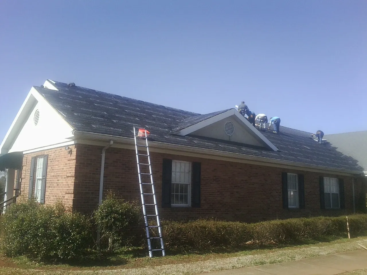 Crew tearing shingles off a brick ranch roof with a ladder set — Metal Roof Repair work by our crew in Fort Mill