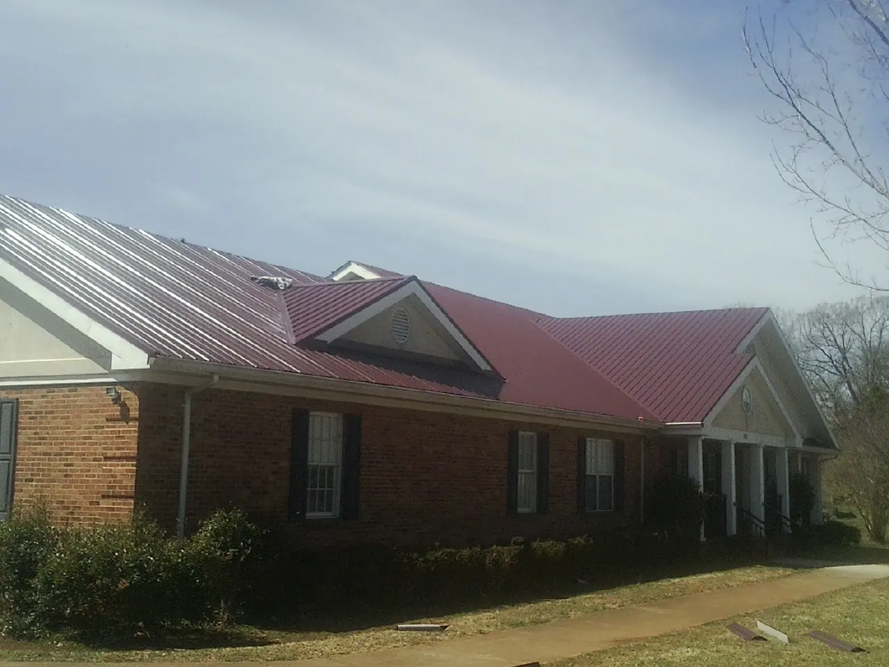 Red metal roof with gabled entries on a long brick building, from a Hail Damage Roof Repair job in Fort Mill