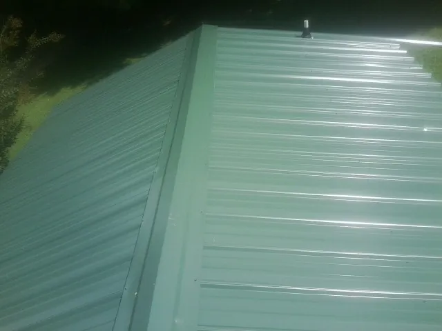 New green metal panels meeting at the ridge of a roof — Flat Roof Repair work by our crew in Fort Mill