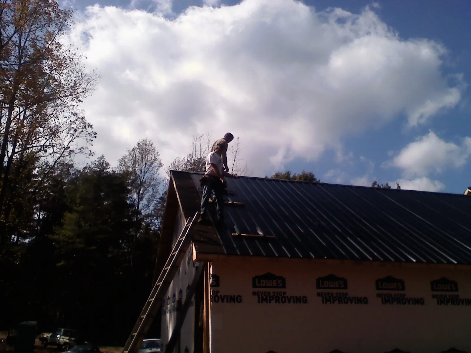 Roofer fastening dark metal panels high against a cloudy sky, from a Roof Inspection job in Fort Mill