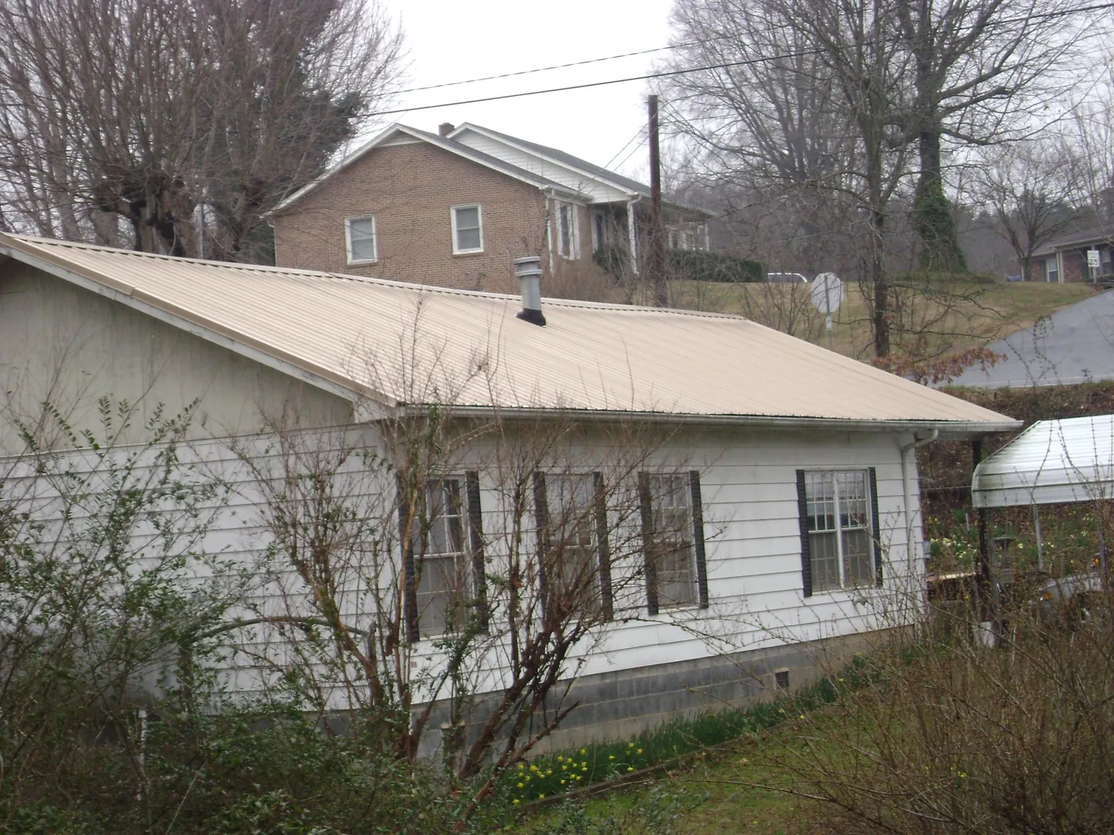 Tan metal roof on a white sided house set into a hillside — Commercial Roofing by Roofing Brothers in Fort Mill